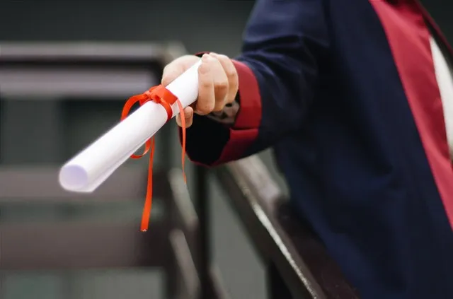 person wearing black graduation gown handing diploma to another person