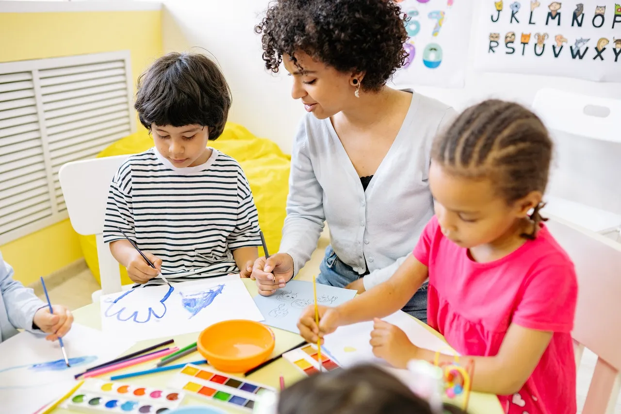 Preschool students painting with watercolors with their teacher